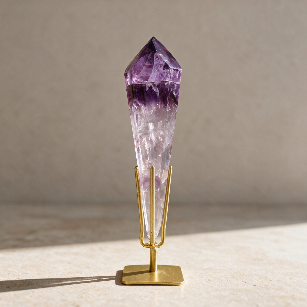 Polished amethyst scepter wand upright in its gold metal stand on a pale plaster surface in daylight