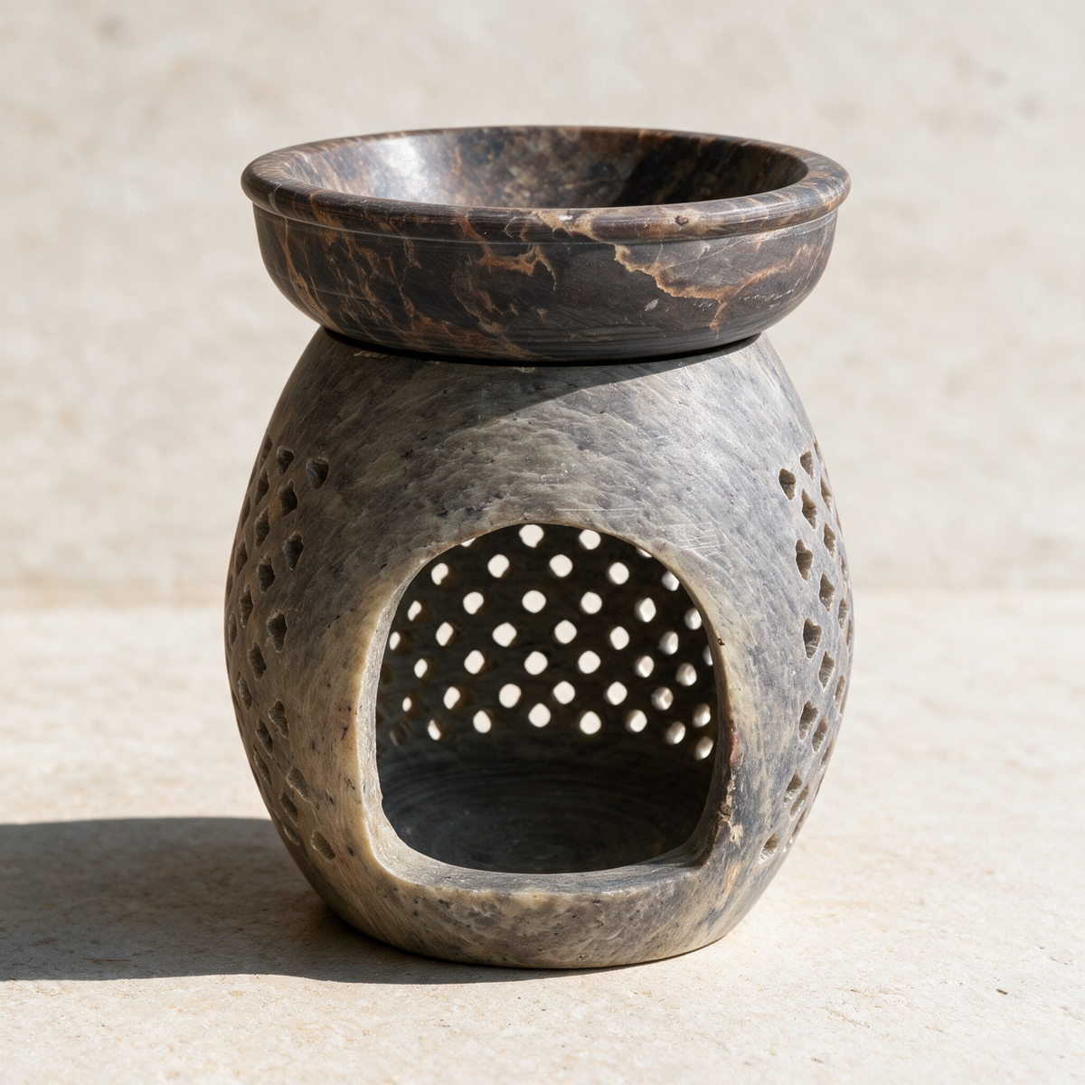 The soapstone burner on pale plaster, the dark marbled dish seated on top above an arched opening and a lattice of round holes.