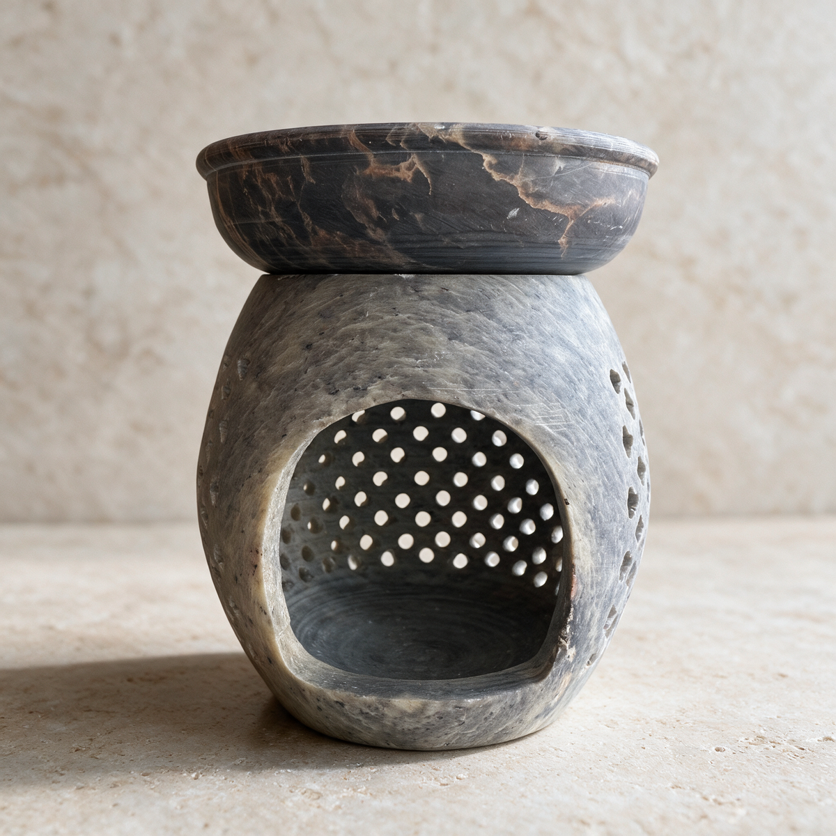 The round-hole soapstone burner on pale stone, the tealight chamber open at the front beneath the marbled dish.