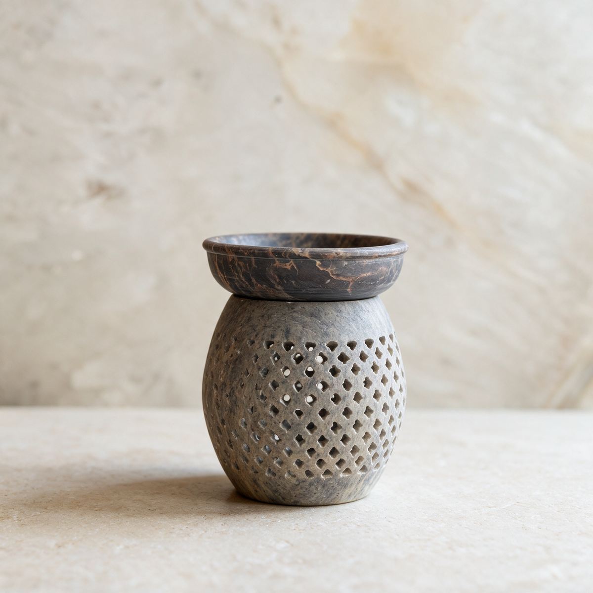 The diamond-lattice soapstone burner standing alone on a pale marble surface, its dish seated on the carved body.
