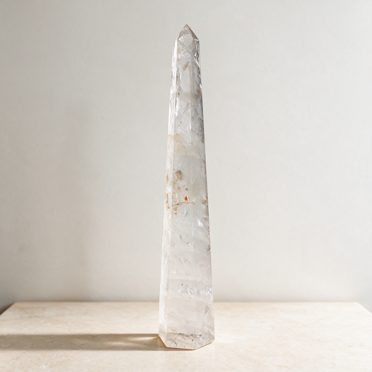 The obelisk against a plain white wall, showing its tapered four-sided form and the veils and inclusions inside the stone.