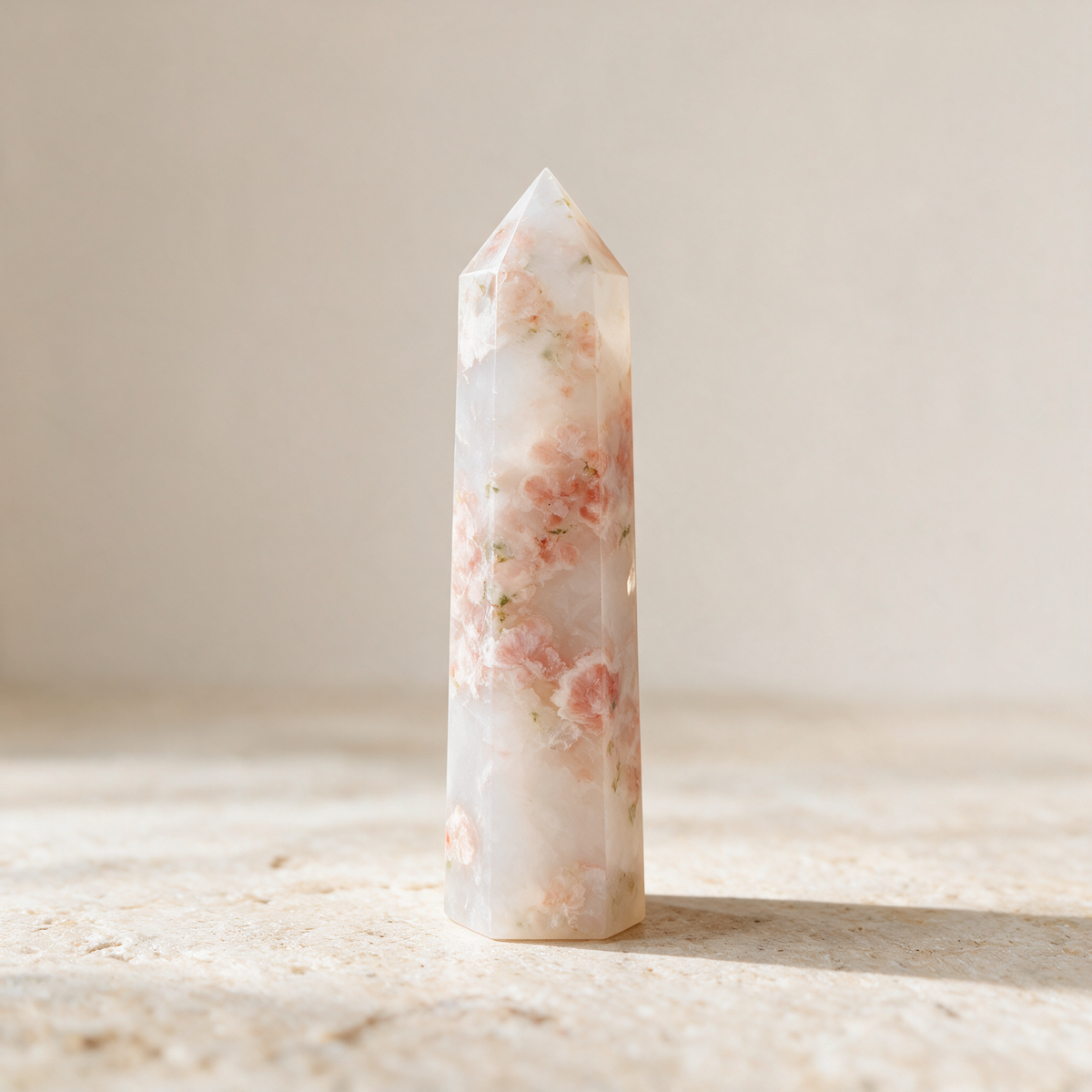 Flower agate tower on a pale stone ledge in soft daylight, blossom-like inclusions scattered up the shaft