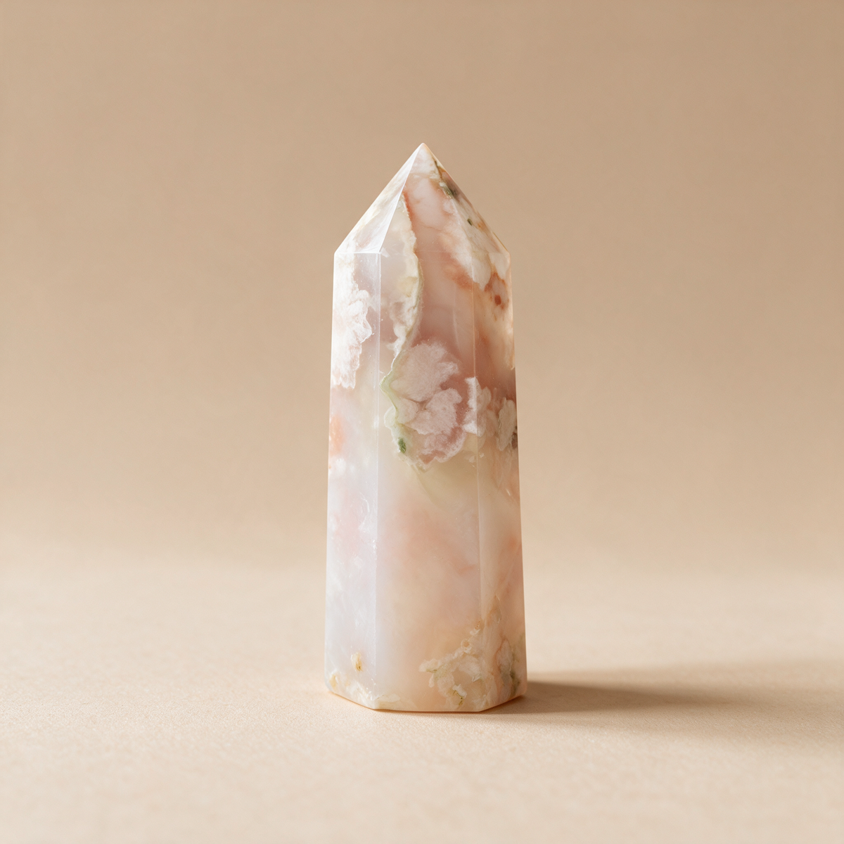 Flower agate tower against a warm beige backdrop, showing the polished faces and pointed tip