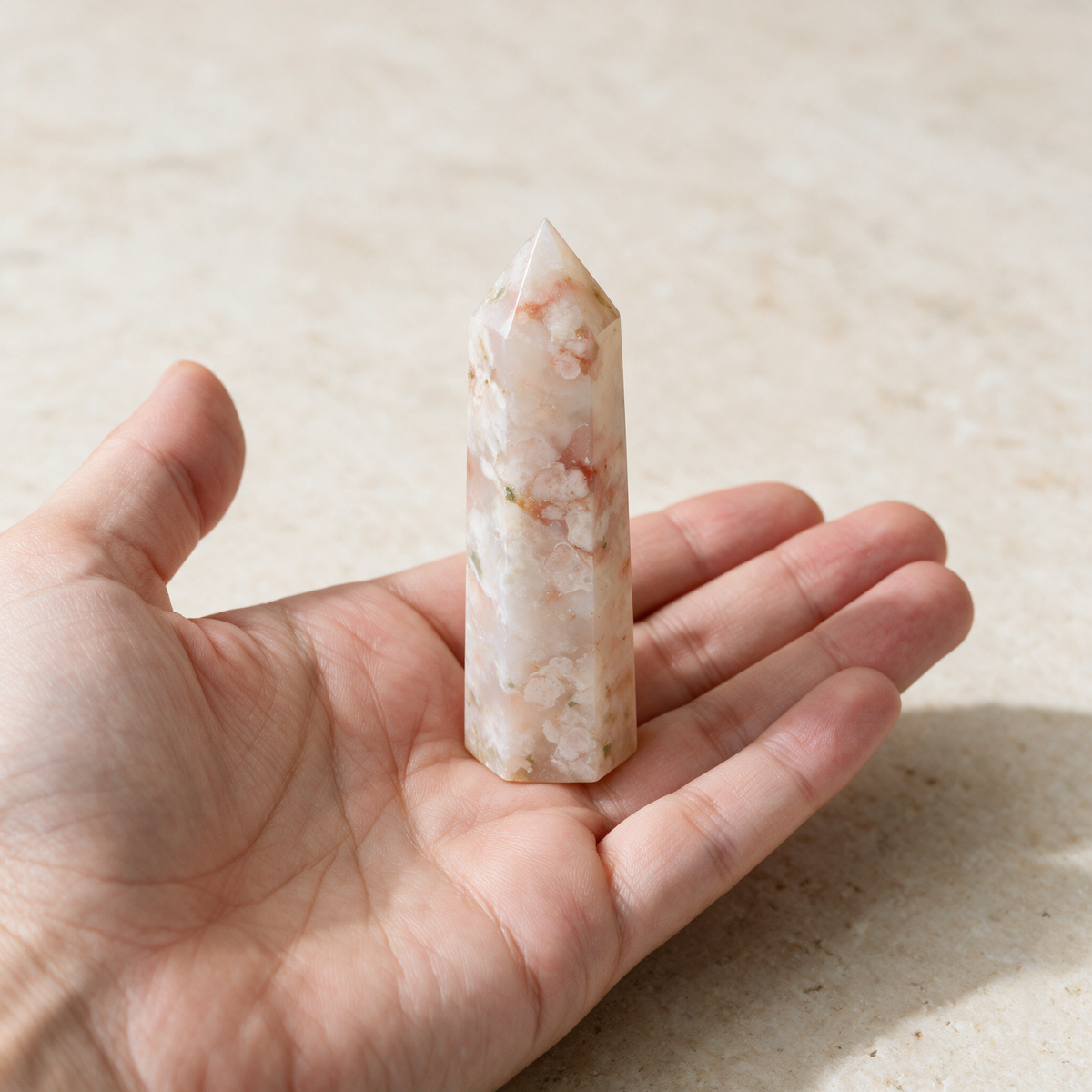 A hand holding the flower agate tower flat on the palm to show its size