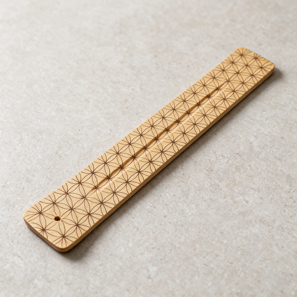 Natural wood incense burner lying flat on a pale surface, the Flower of Life pattern printed along its length and the stick hole at one end