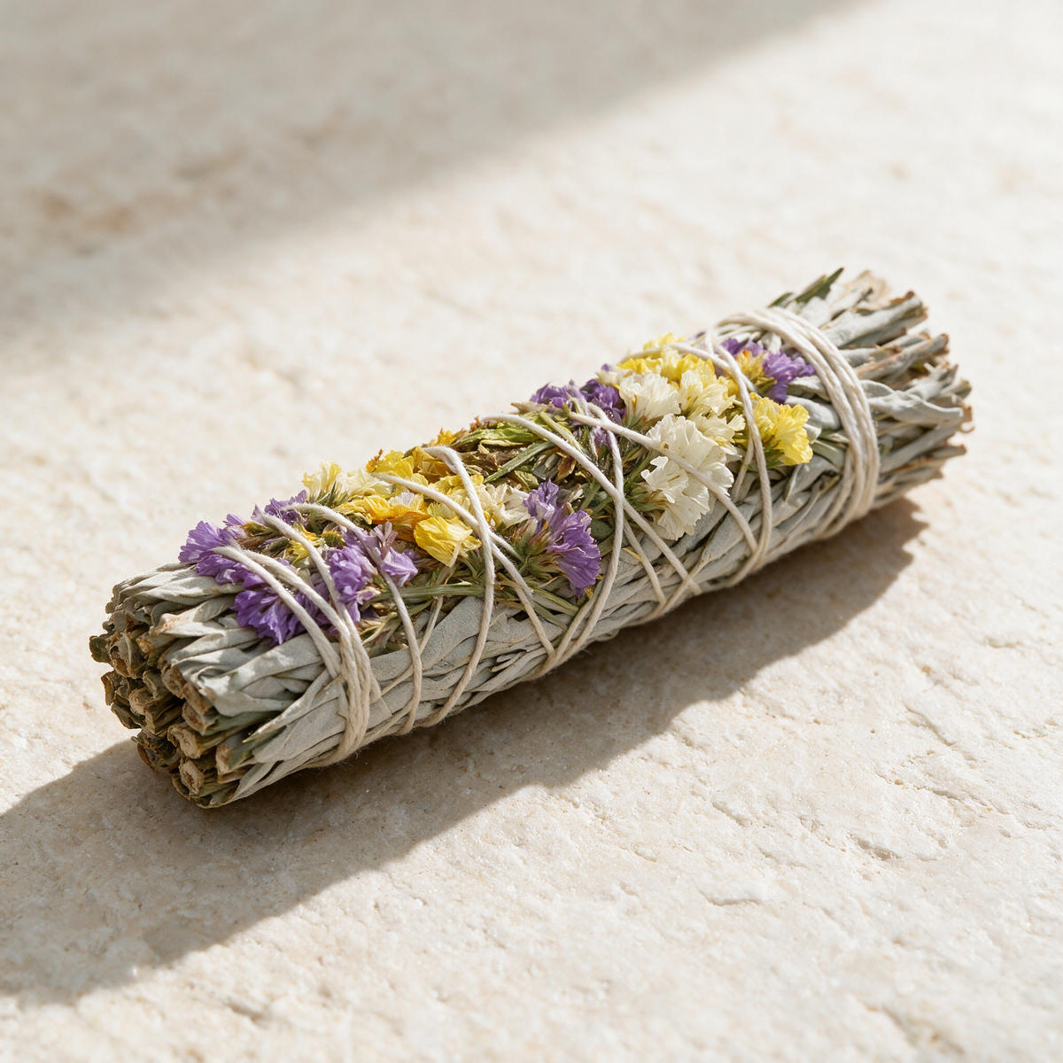 The bundle lying on sunlit travertine, seen from the side, the small dried statice flowers threaded along the binding.