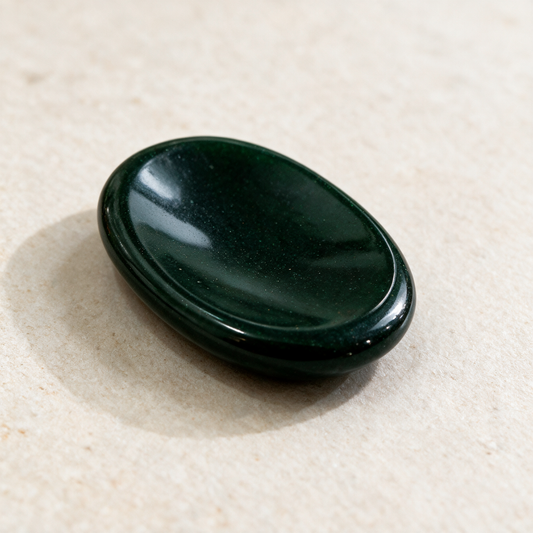 A green goldstone comfort stone on a cream surface, deep bottle-green and highly polished