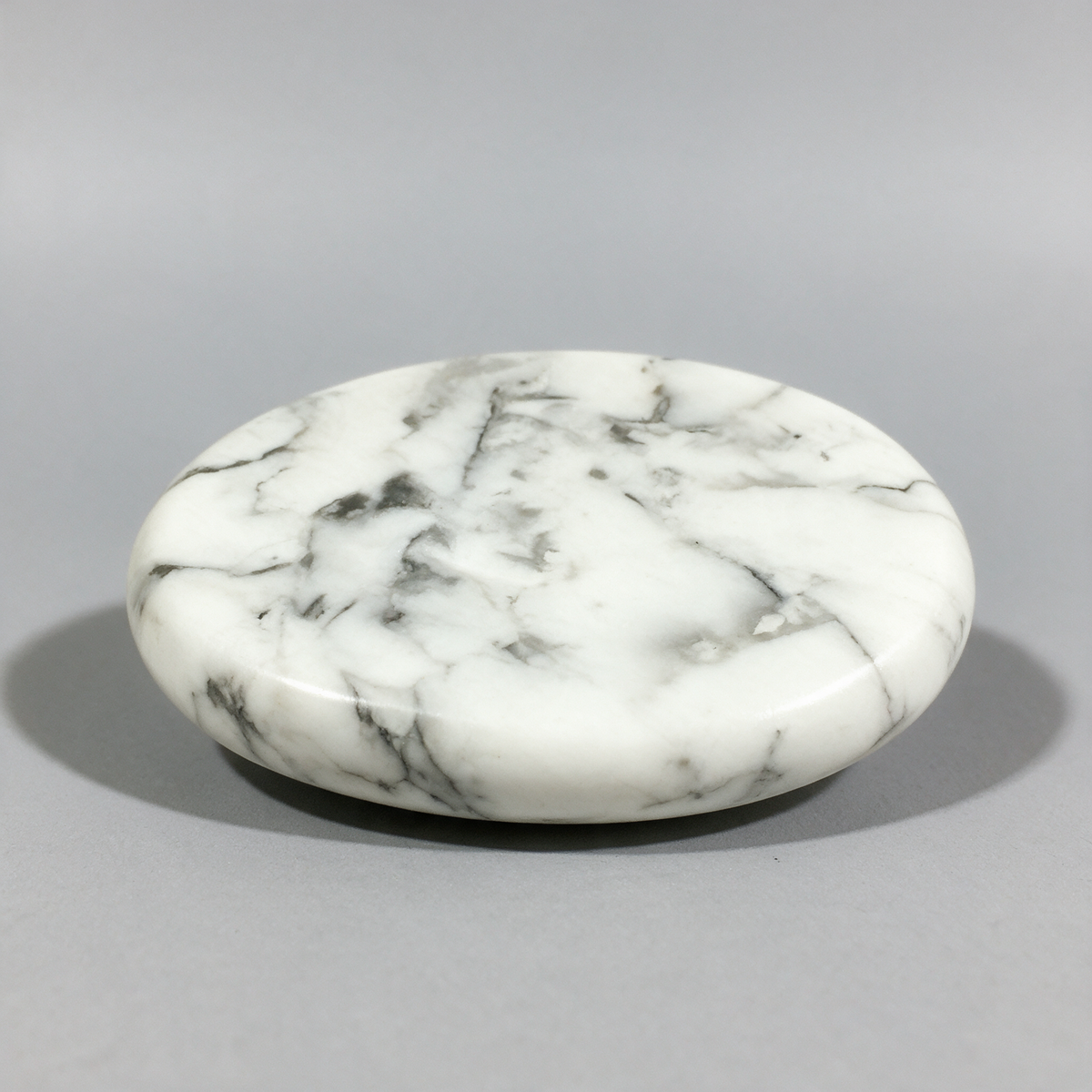 Smooth white howlite palm stone at a low angle, gray veining running across the polished face