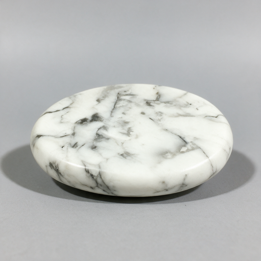 Smooth white howlite palm stone at a low angle, gray veining running across the polished face