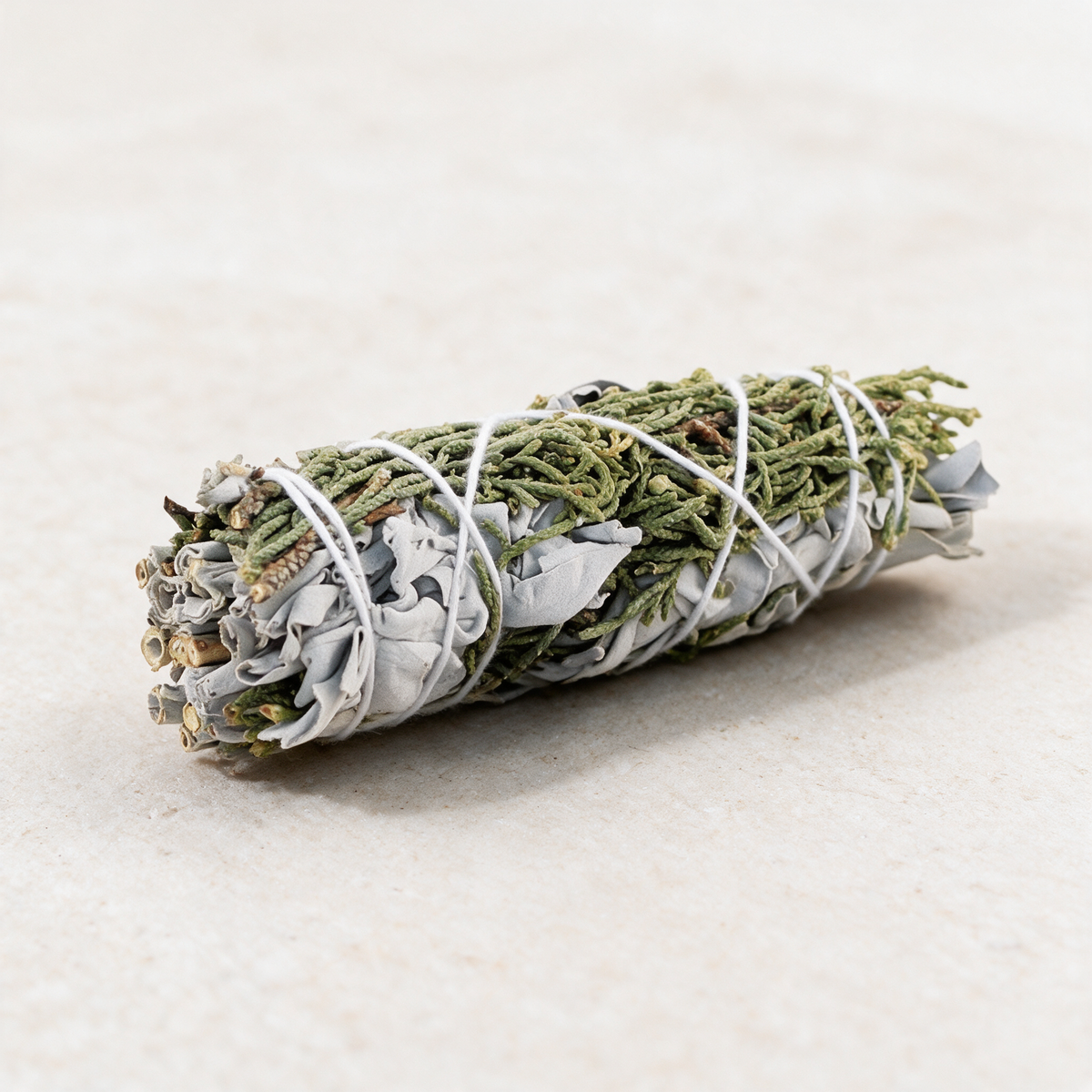 Juniper and white sage smudge stick on a pale stone surface, cut stems facing the camera