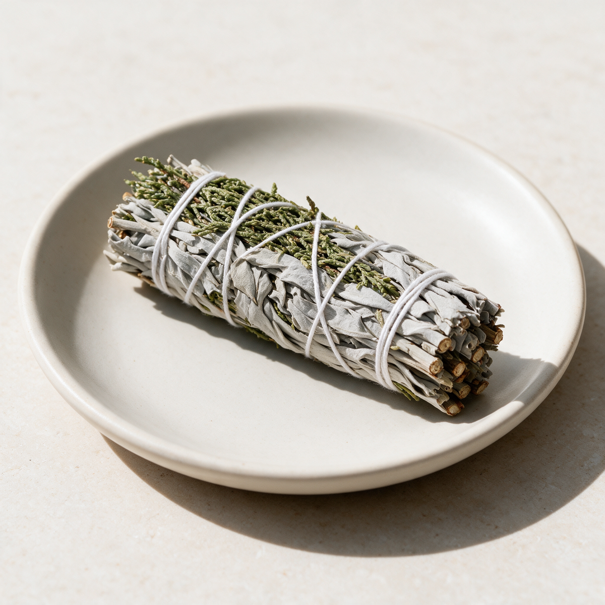 Four-inch juniper and white sage bundle resting on a small cream ceramic dish