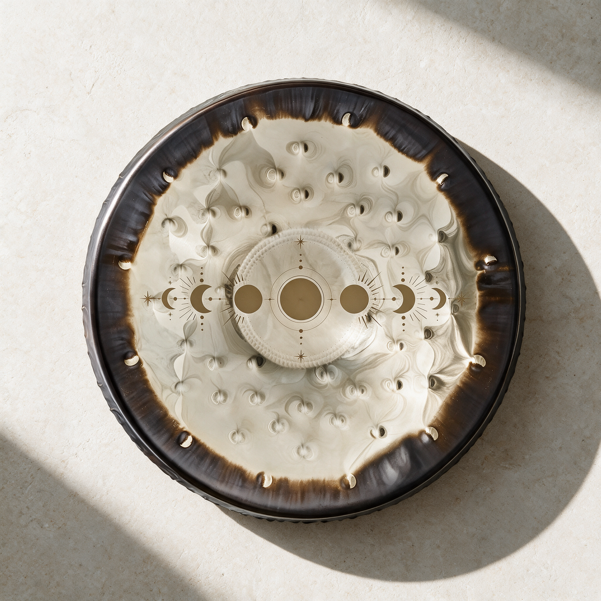 Moon Phases gong resting on a pale surface seen from above, the cream face marked with the lunar cycle and a ring of raised dimples
