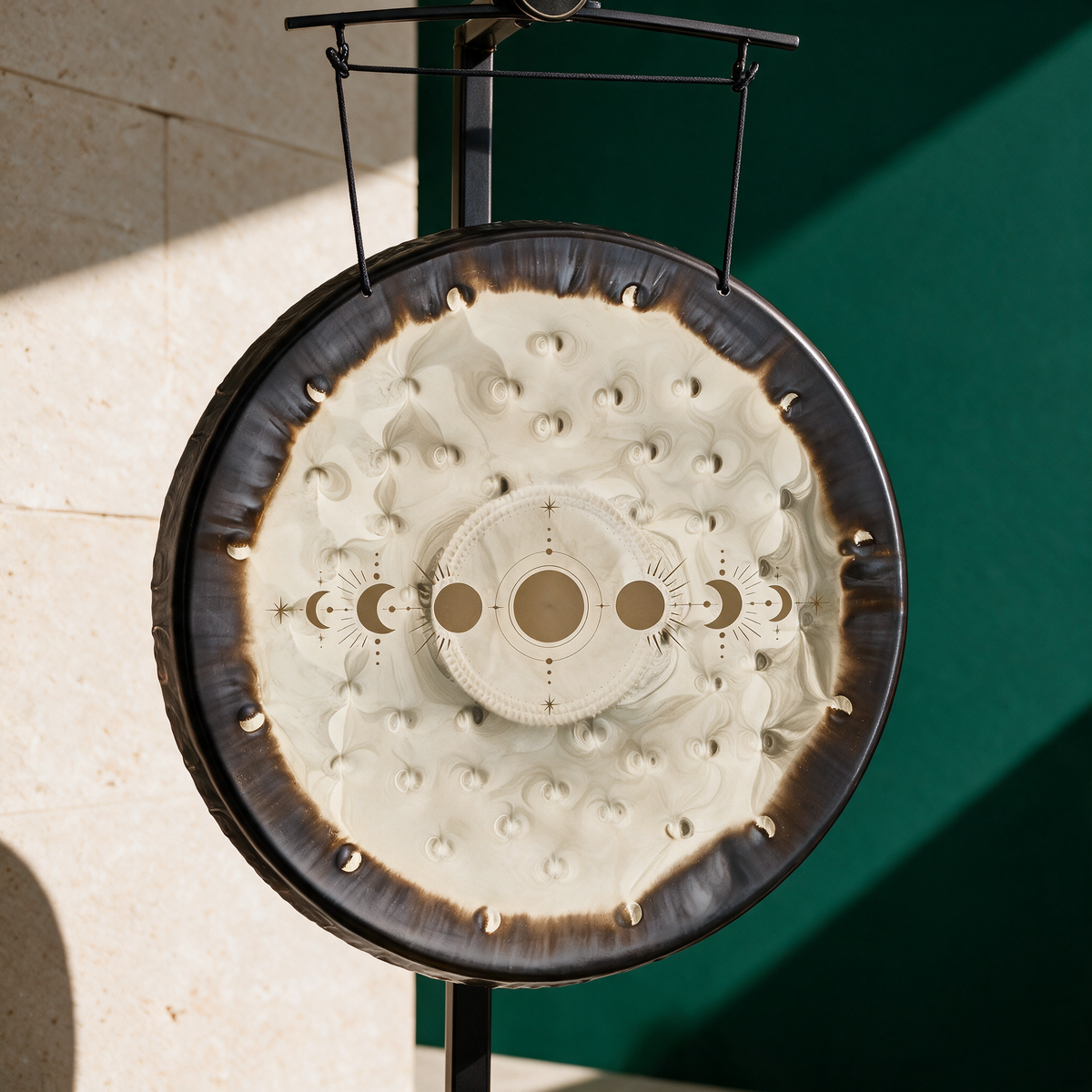 Moon Phases soundscape gong hanging from a black gong stand against a green backdrop, the cream face showing the lunar cycle
