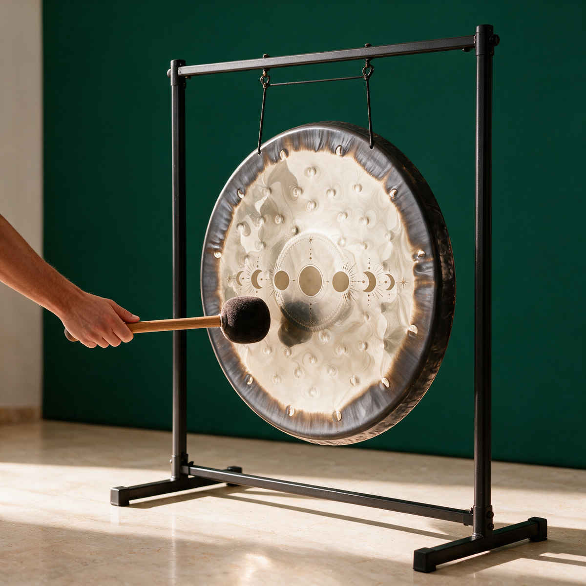 Hand striking the Moon Phases gong with a mallet while it hangs from a black floor stand