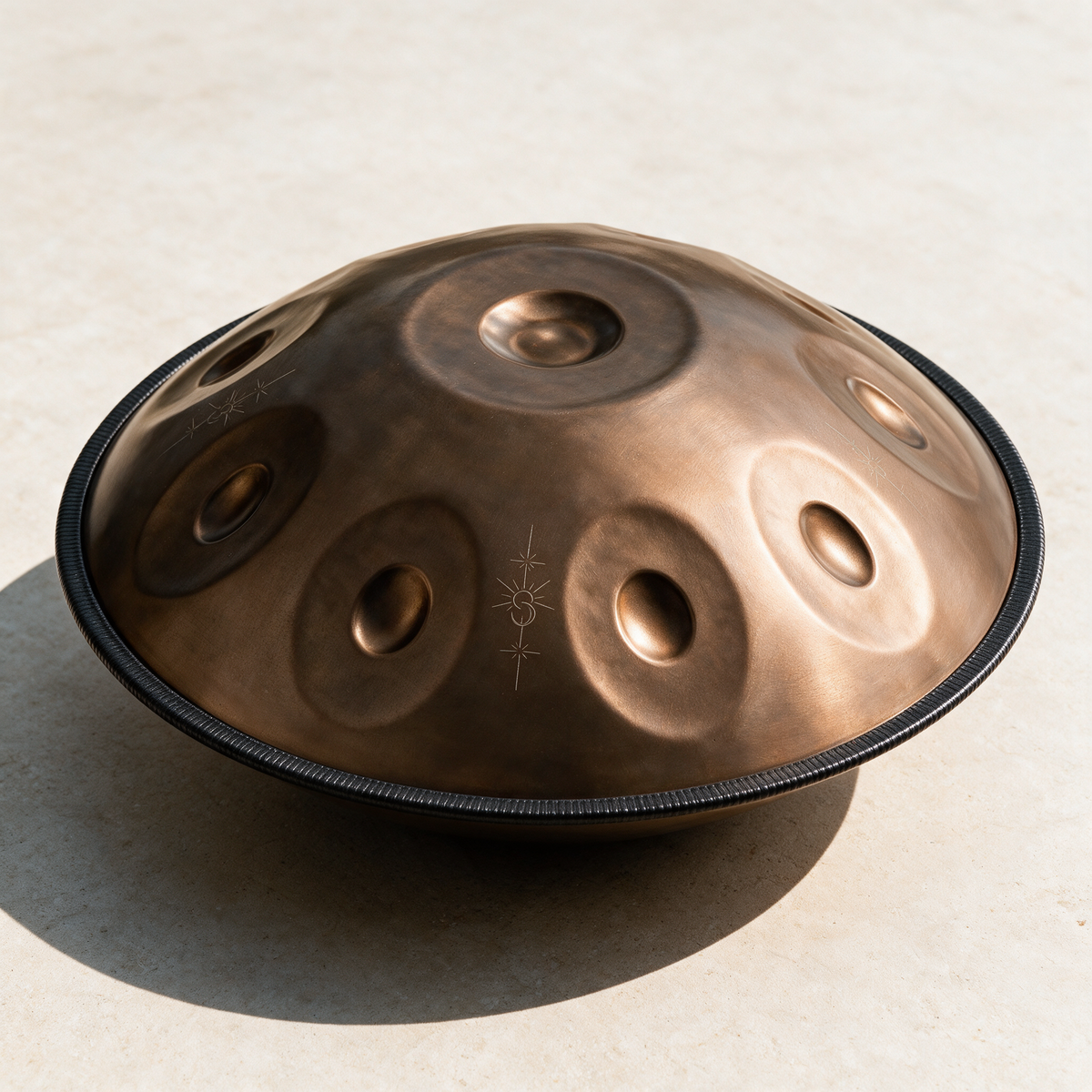 Vintage copper handpan angled on a pale stone surface in daylight, showing the tone fields and the dark rim seam
