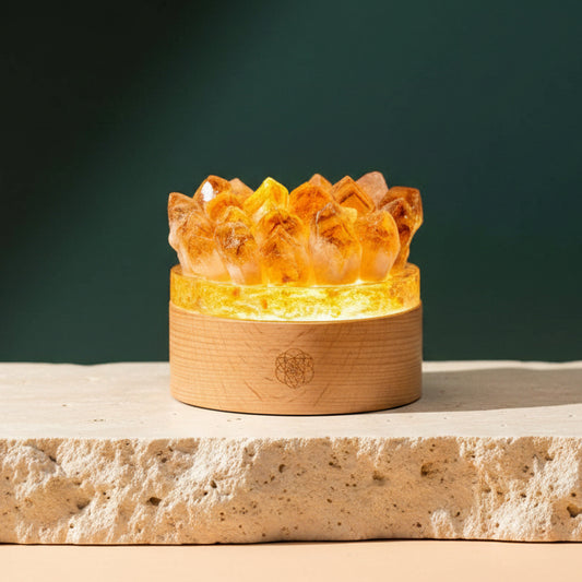 Citrine crystal lamp lit from within on a pale stone ledge, raw golden points set around a round wooden base.