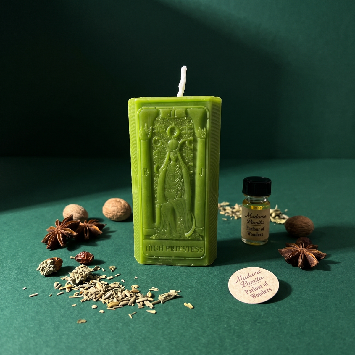 The High Priestess beeswax tarot candle in green with the kit oil and herbs on a teal backdrop