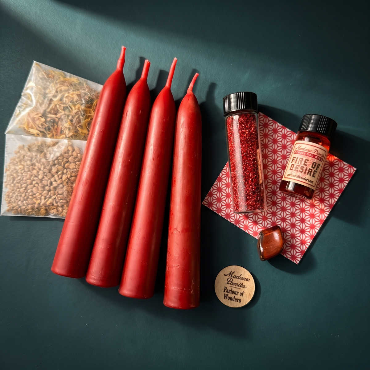 Passion Candle Spell Booster Pack flat lay with four red beeswax taper candles, oil, glitter, herbs and petition paper on a teal backdrop