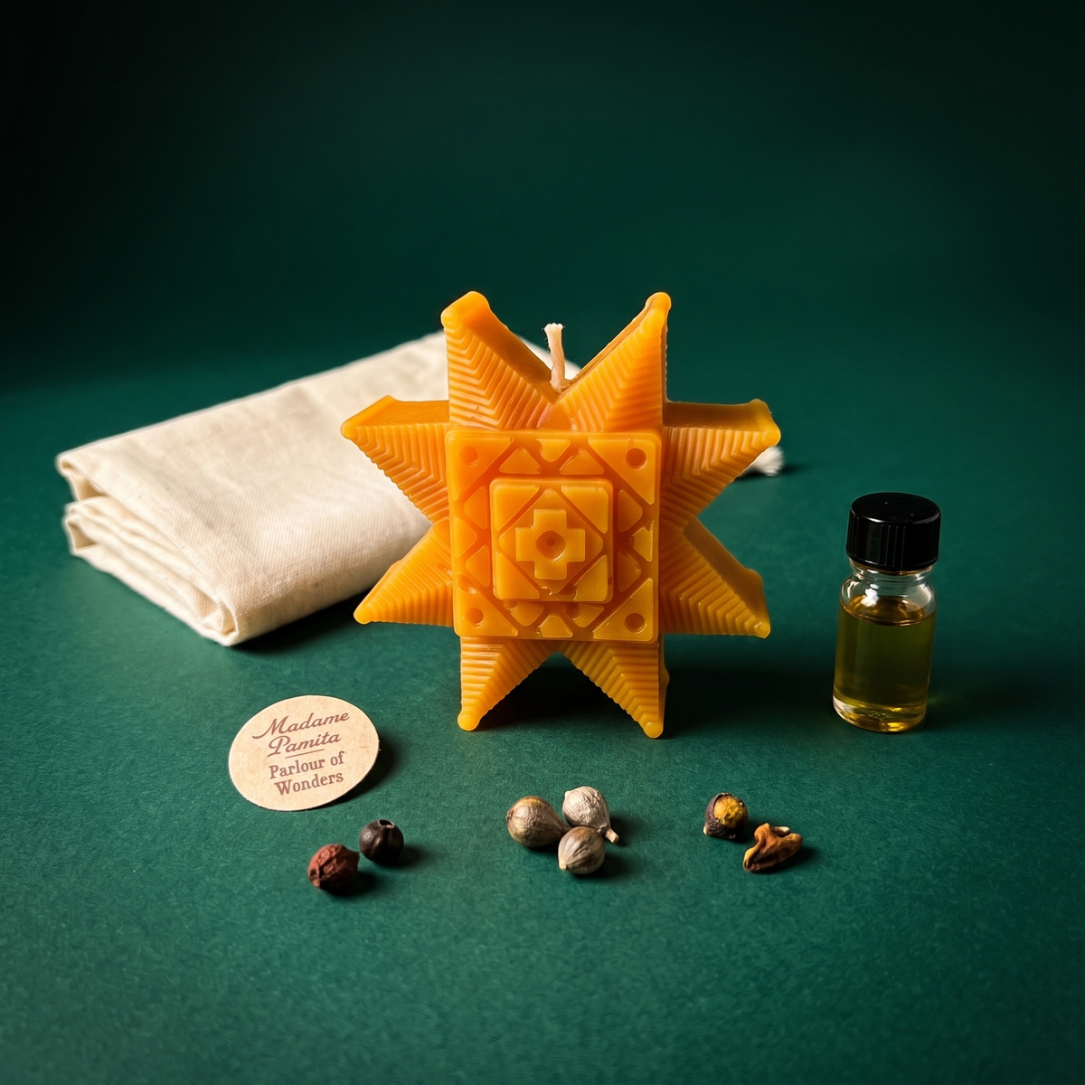 Burst of Brilliance Ruzha kit on green: the orange eight-pointed beeswax star candle with a folded cotton bag, spiritual oil bottle, loose herbs and the Madame Pamita maker's tag