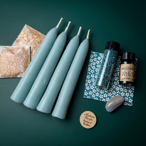 Communication Candle Spell Booster Pack on a deep green backdrop: four pale blue beeswax tapers, a vial of teal glass glitter, a Talk to Me ritual oil bottle, a teal floral card, two herb packets, a gray-lavender tumbled stone and a wooden Madame Pamita token from Parlour of Wonders.