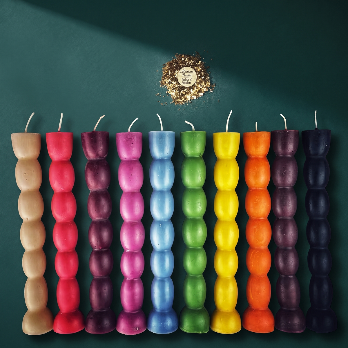 All ten colors of the seven knob candle stood side by side against a dark green wall, each a column of seven stacked knobs, with the Madame Pamita label and herbs above them.